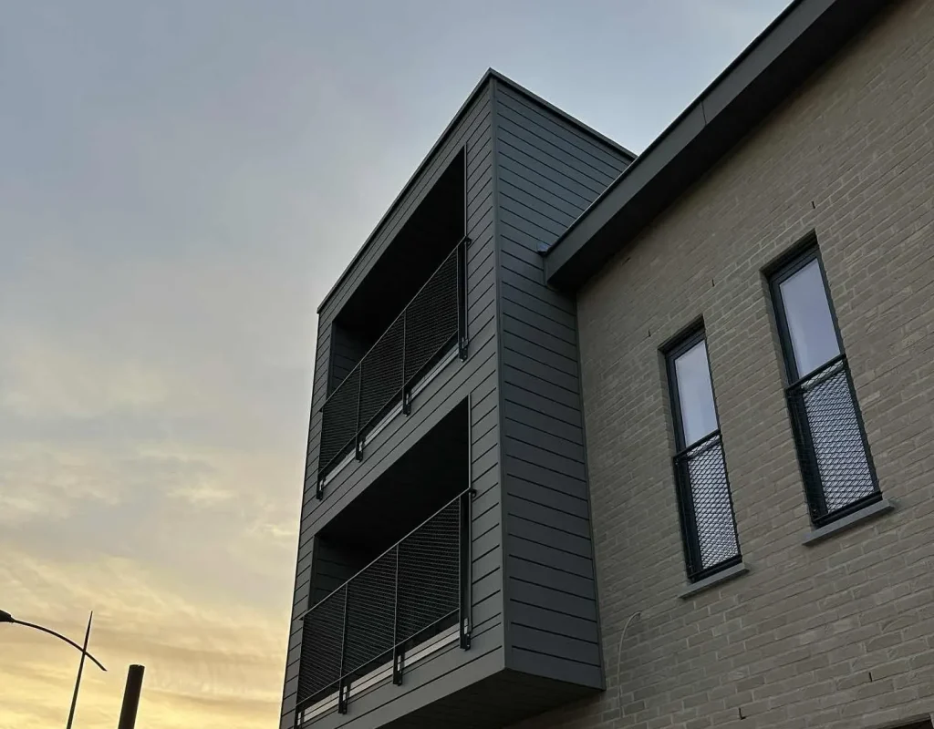 Balcons métalliques superposés avec garde-corps grillagés sur façade en bardage, réalisation Metal Hanart au coucher du soleil